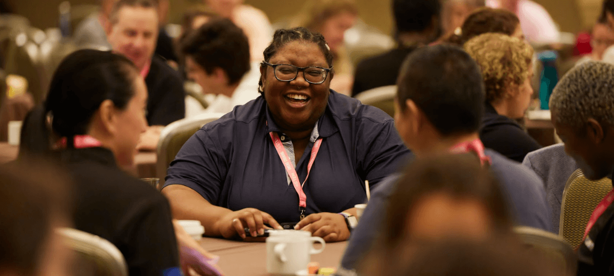 oSTEM conference attendees sitting around a table, with the camera focused on one attendee with a wide smile.